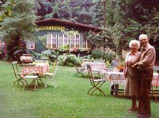 Mosthof im Hintergrund, davor einige bestuhlte Tische, rechts älteres Ehepaar